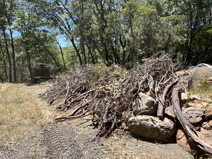 A long pile of cut brush and limbs along a gravel road, with R2's machine behind it