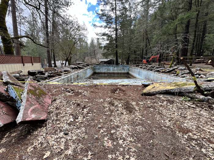 Logs laid into an old swimming pool for a hugelkultur project, later topped with chips and compost