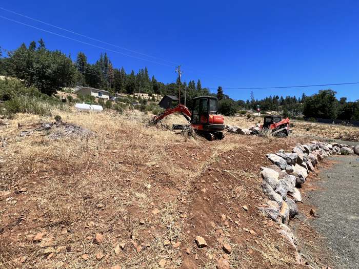 R2's excavator clearing a burned lot and setting a rock border