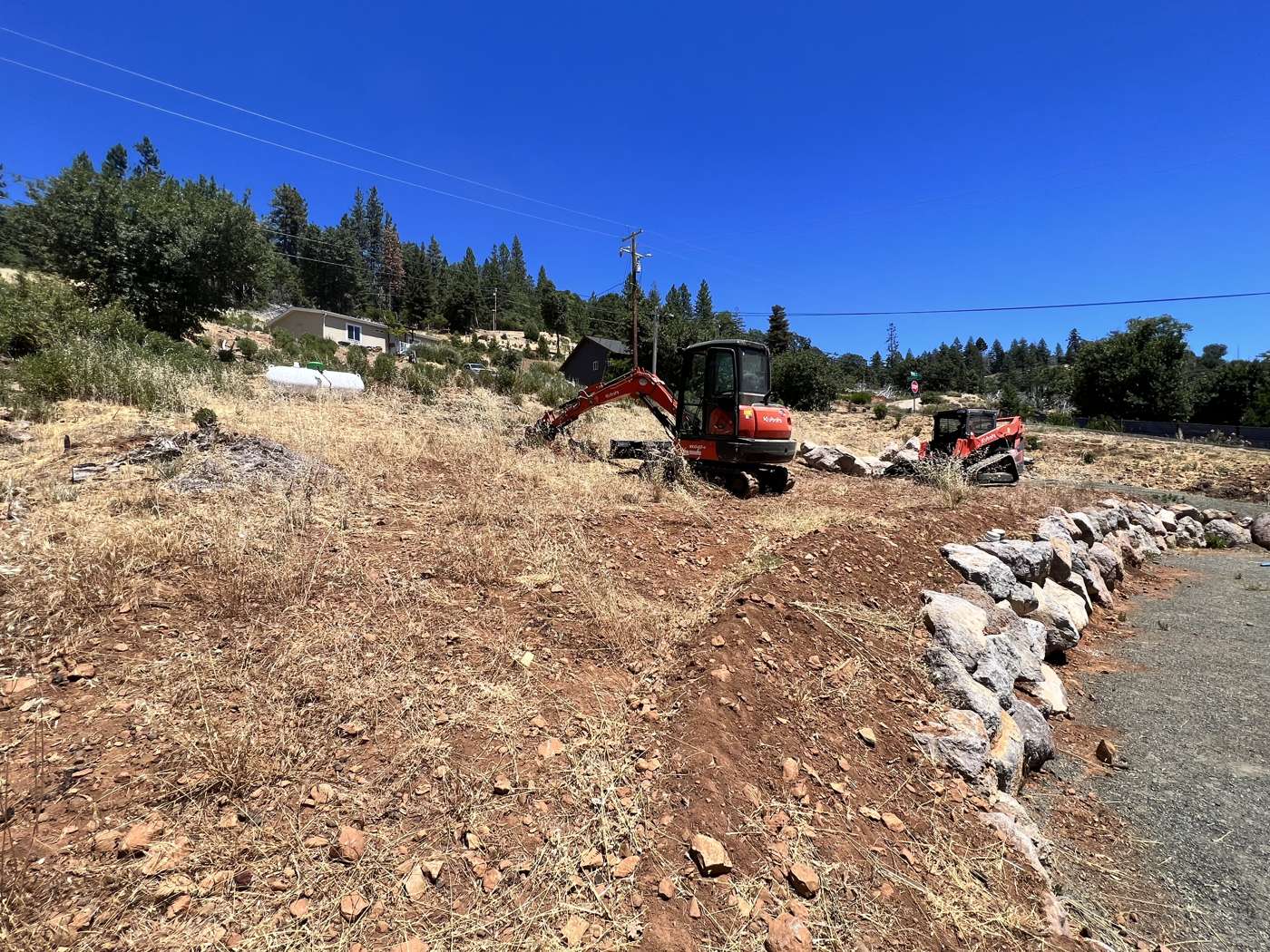 R2's excavator clearing a burned lot and setting a rock border