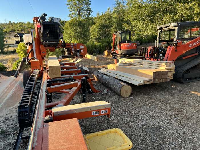 R2's sawmill with fresh milled lumber, a skid steer and an excavator in the yard