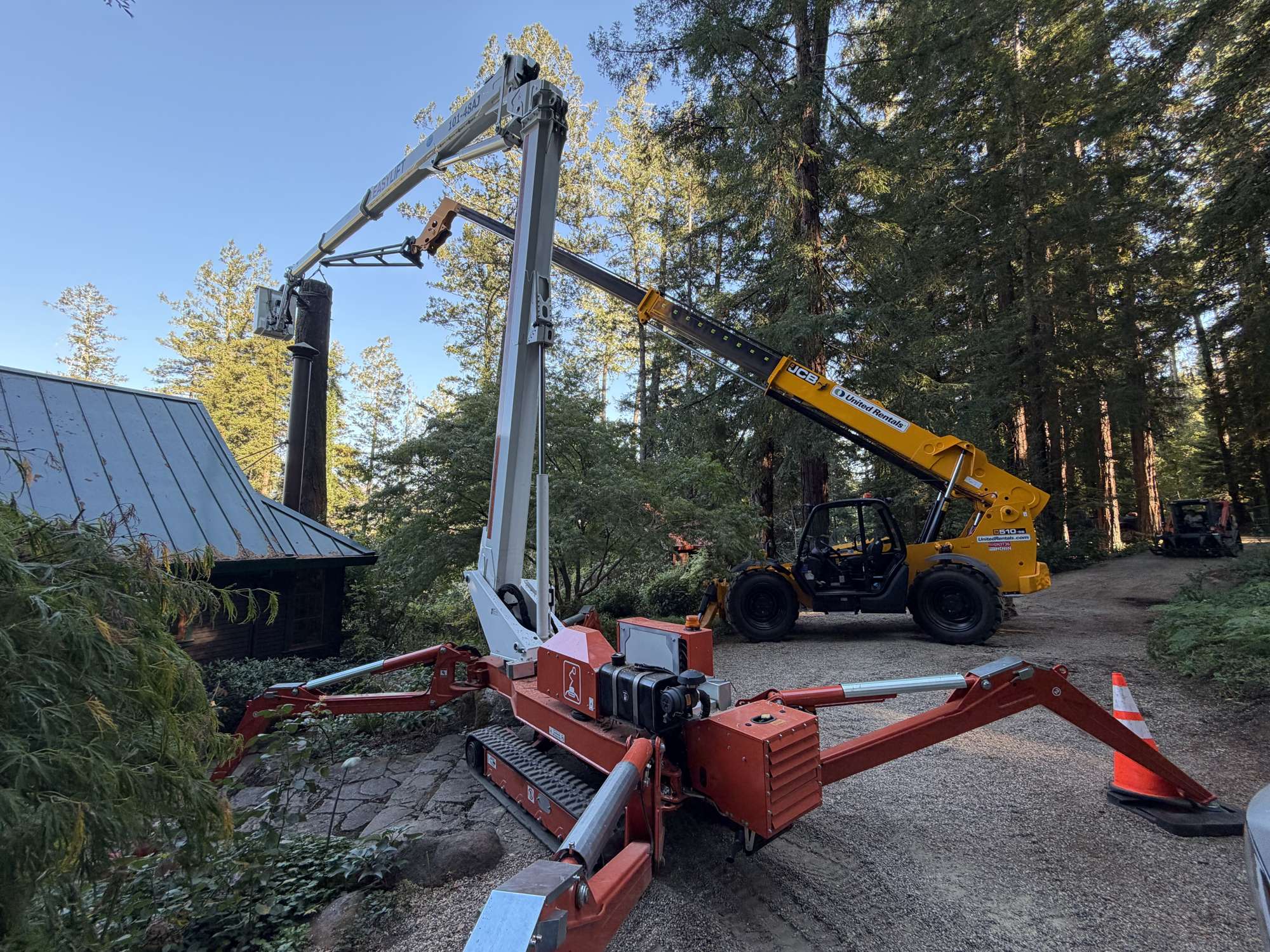 R2's tracked spider lift beside a cabin in Calistoga while a telehandler lowers a section of a big fir