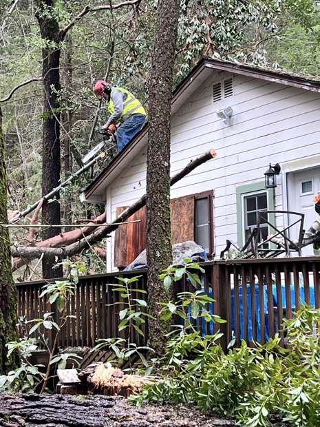 An R2 crew member on a roof cutting a fallen tree into pieces