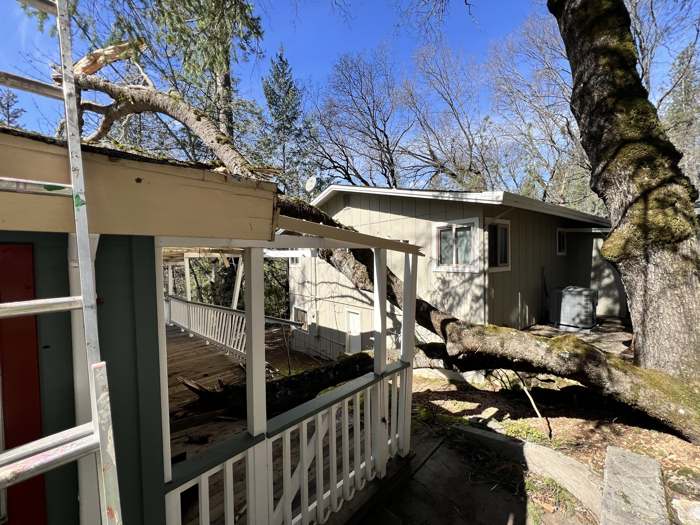 A big oak limb lying across a porch roof and railing