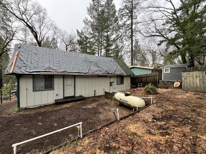 A house with its roof tarped and the yard cleared after a storm tree came off it