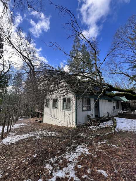 A broken tree lying across the roof of a white house after a snow storm