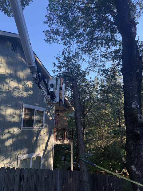 R2's spider lift boom reaching up beside a two-story house into a pine